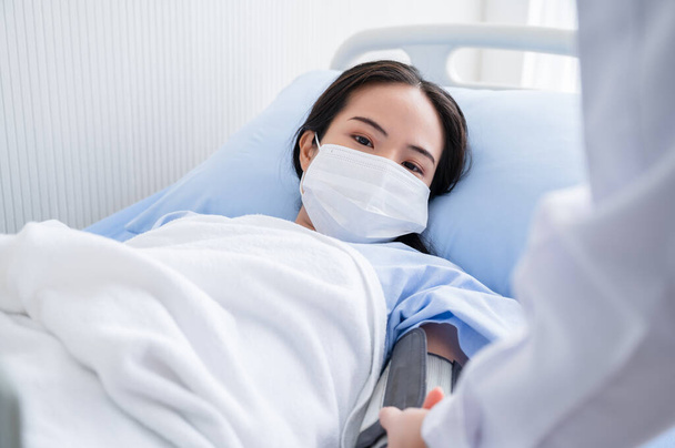 Jonge vrouw op het ziekenhuisbed met een masker om de bloeddruk te controleren tijdens de uitbraak van het coronavirus 19. Concepten om de verspreiding van COVID-19 te voorkomen. - Foto, afbeelding
