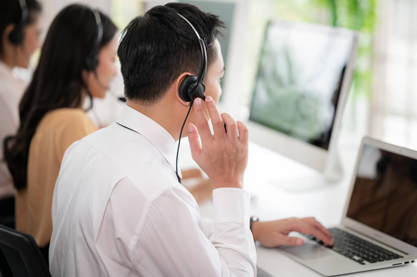 Callcenter-Mitarbeiter in Asien tragen Kopfhörer mit Mikrofon. Lächeln Sie, während Sie Kunden an Schreibtischen und Computern bedienen. Servicekonzept und Beratung. Kommunikationskonzept. - Foto, Bild