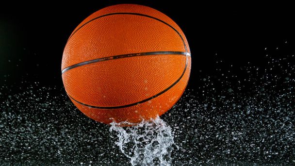 Pelota de baloncesto cayendo en la superficie del agua, fondo negro. - Foto, imagen