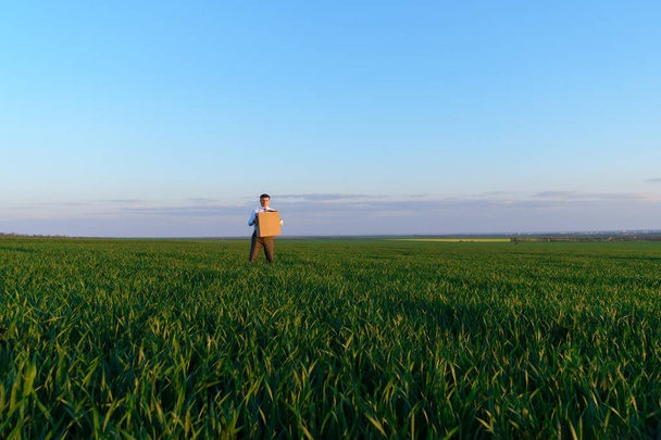 przedsiębiorca trzyma kartonowe pudełko i pozuje na zielonym polu trawiastym - koncepcja biznesowa - Zdjęcie, obraz