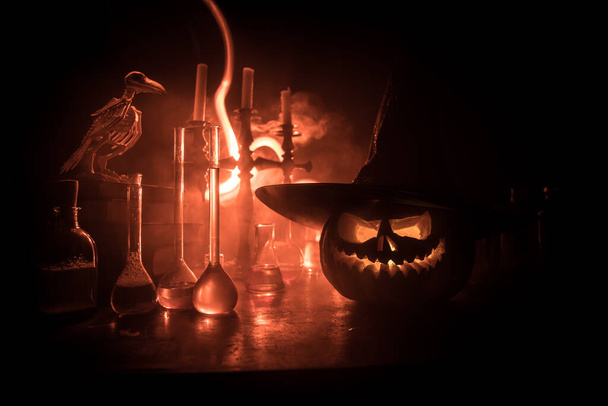Wizard's Desk. Horror Halloween concept. Magic potions in bottles on wooden table with books and candles. Halloween still-life background with different elements on dark toned foggy background. Selective focus - Photo, Image