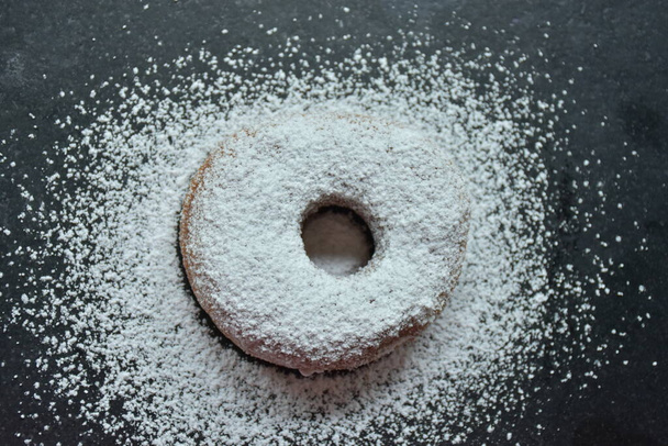 donut e açúcar em pó sobre um fundo preto, - Foto, Imagem