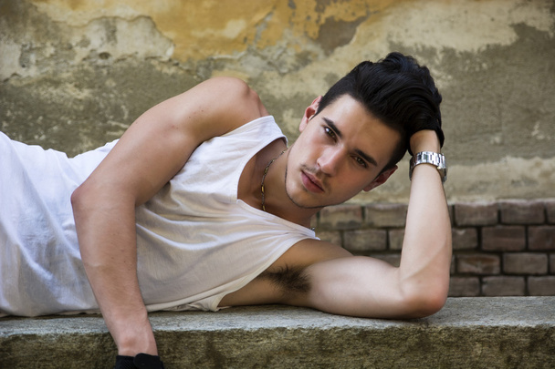 Attractive young man laying down, outdoors, looking at camera - Fotoğraf, Görsel