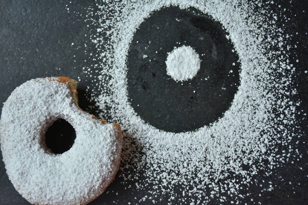 ντόνατ και ζάχαρη άχνη σε μαύρο φόντο, - Φωτογραφία, εικόνα