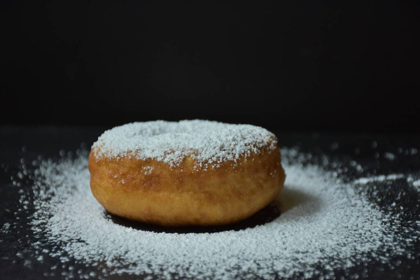 Donut und Puderzucker auf schwarzem Hintergrund, - Foto, Bild