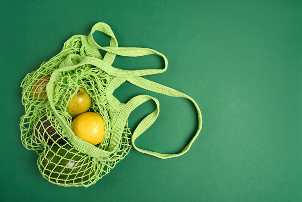 Green string eco shopping bag with vegatables avocado, lemon on green background - Photo, Image