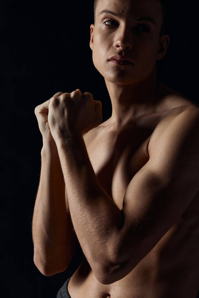 sportovní chlap s čerpané paže svaly na černém pozadí při pohledu do strany zblízka  - Fotografie, Obrázek