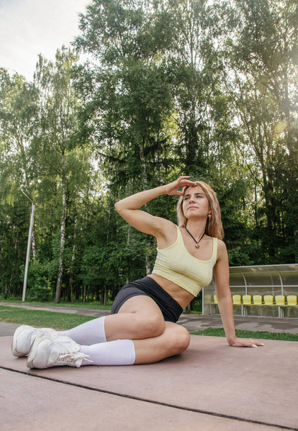 portrait of a blonde girl in a sports uniform black leggings and a yellow crop top sitting on a ping pong table - Foto, immagini