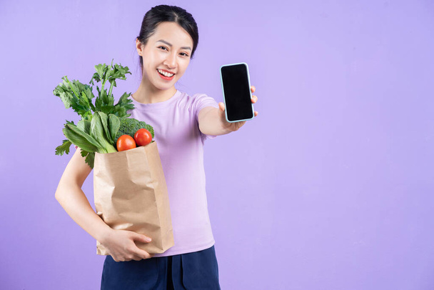 紫の背景に野菜袋を持っている若いアジアの女性 - 写真・画像