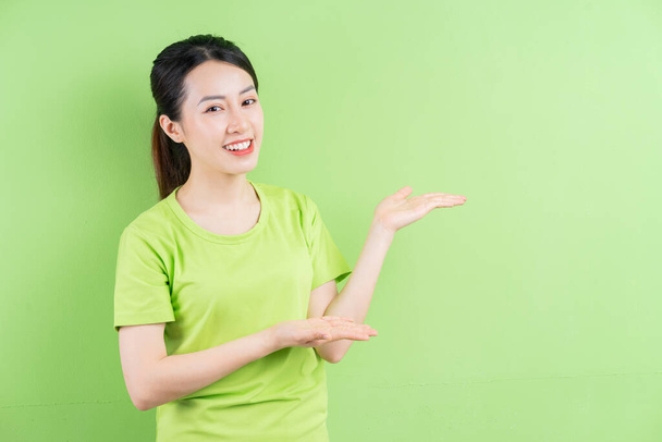 若いアジアの女性は緑のシャツを着て、緑の背景にポーズ - 写真・画像