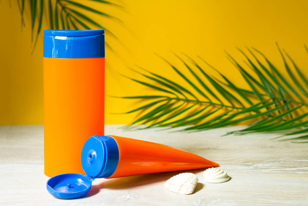Tubes with mock up sunscreens on the table with yellow summer background. UV protection of the skin with an SPF filter, hair care-shampoo and conditioner. A safe tan on the beach, resort on the sea. - Photo, Image