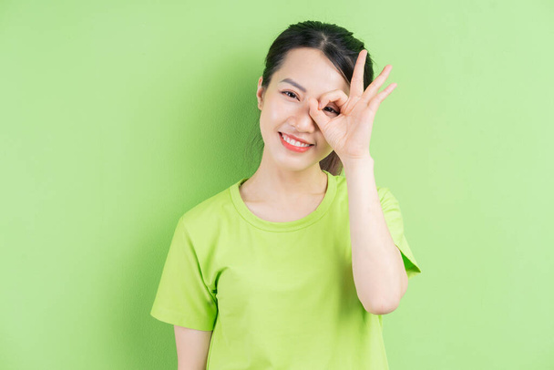 Νεαρή Ασιάτισσα που φοράει πράσινο πουκάμισο και ποζάρει σε πράσινο φόντο - Φωτογραφία, εικόνα