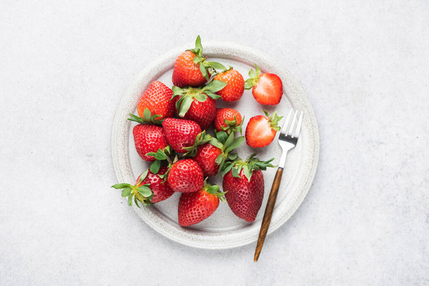 Strawberries on a ceramic plate, grey concrete stone background, top view. Summer berries - Foto, Imagen