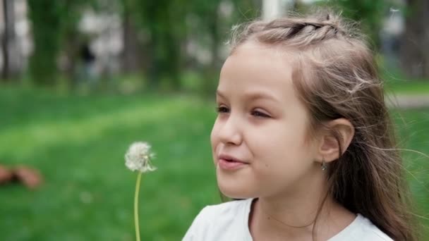 Portret pięknej nastolatki wiejącej na dojrzałym dmuchawcu w parku wiosennym lub letnim. zwolniony film wideo - Materiał filmowy, wideo
