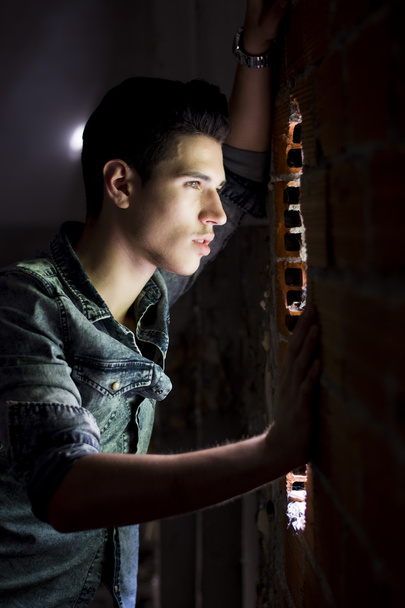 Young man looking through hole in brick wall - Foto, afbeelding