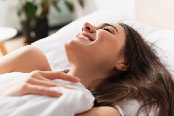 задоволена молода жінка посміхається лежачи на ліжку
 - Фото, зображення
