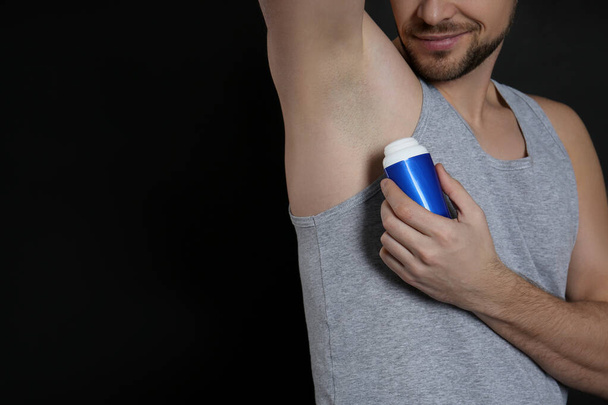 Man applying deodorant on black background, closeup. Space for text - Zdjęcie, obraz