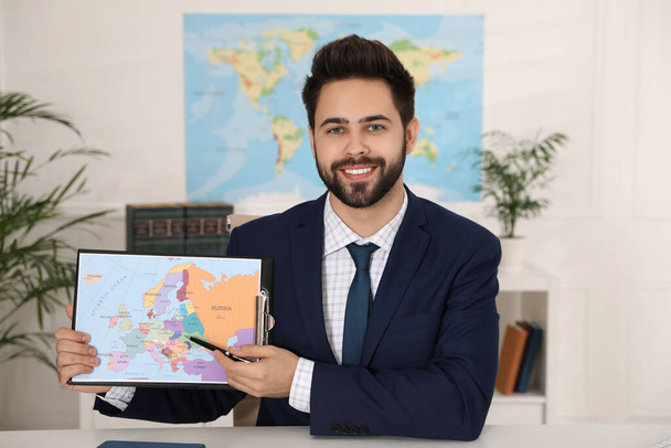 Happy manager showing map at desk in travel agency - Photo, image