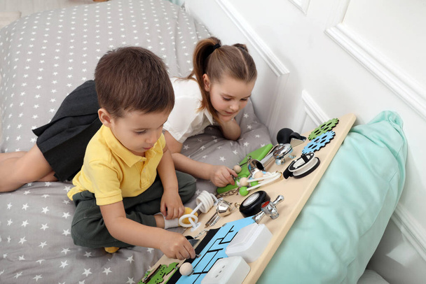 Little boy and girl playing with busy board on bed indoors - Foto, Imagem