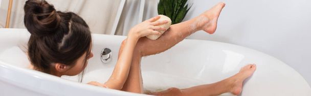 mujer joven con moño de pelo tomando baño con esponja en la bañera, pancarta - Foto, Imagen