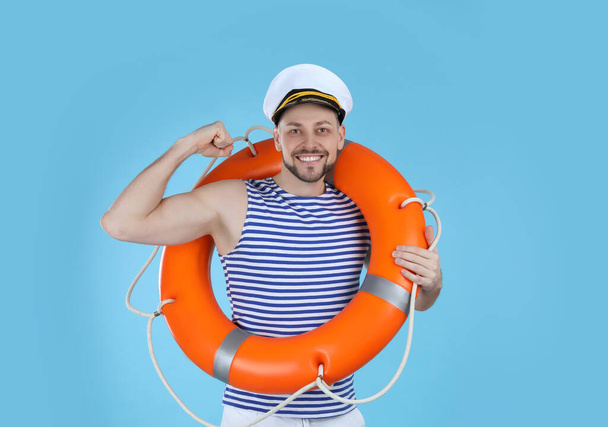 Sailor with orange ring buoy showing biceps on light blue background - Фото, изображение