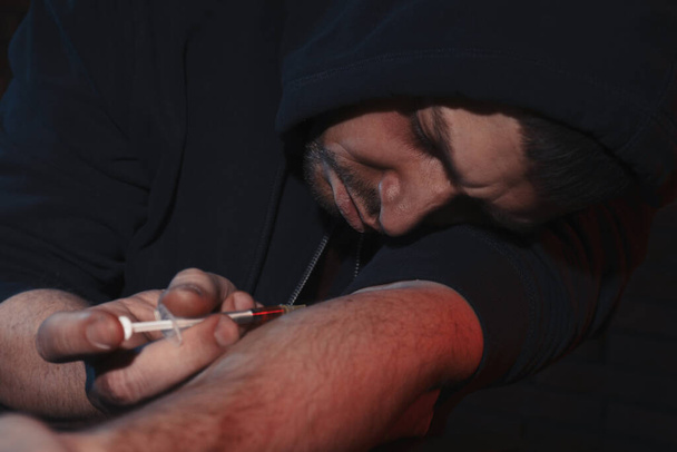 Addicted man taking drugs on dark background - Foto, imagen
