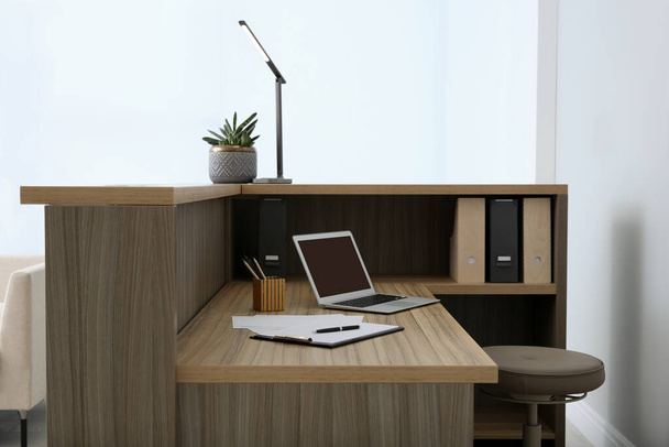 Stylish modern wooden desk with laptop indoors. Receptionist workplace - 写真・画像
