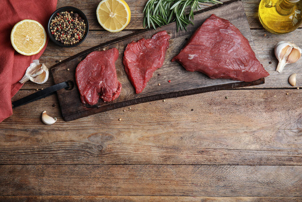 Fresh raw meat steaks and spices on wooden table, flat lay. Space for text - Photo, Image