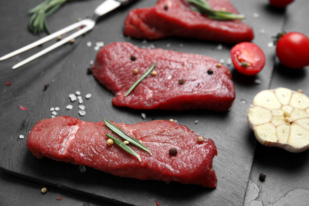 Fresh raw meat steaks and spices on black table, closeup - Photo, image