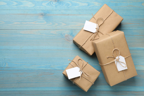 Parcels wrapped in kraft paper with tags on light blue wooden table, flat lay. Space for text - Fotografie, Obrázek