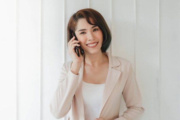Happy Asian working woman is having a smartphone conversation. - Photo, image