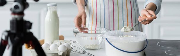 partial view of woman in apron holding spoon with flour near blurred digital camera, banner - Foto, Imagen