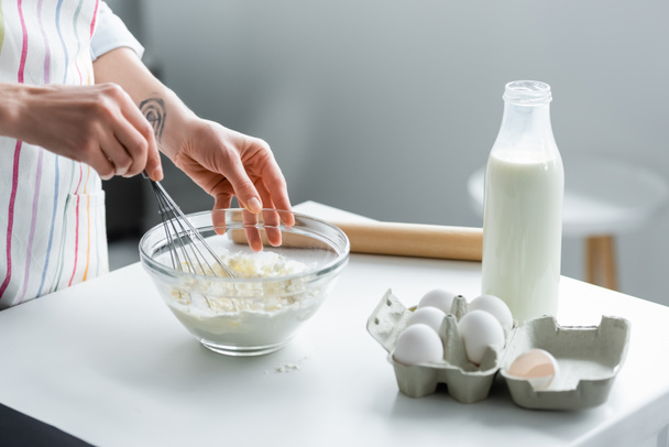 oříznutý pohled na ženu připravující těsto v misce u mléka a kuřecích vajec - Fotografie, Obrázek