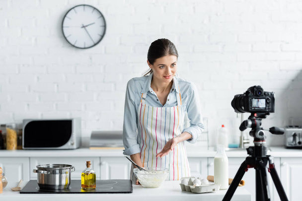 giovane casalinga che punta a ciotola con farina vicino alla fotocamera digitale durante la cottura online - Foto, immagini