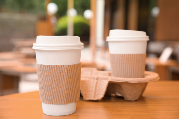 Takeaway paper coffee cups with plastic lids, sleeves and cardboard holder on wooden table outdoors - Photo, image