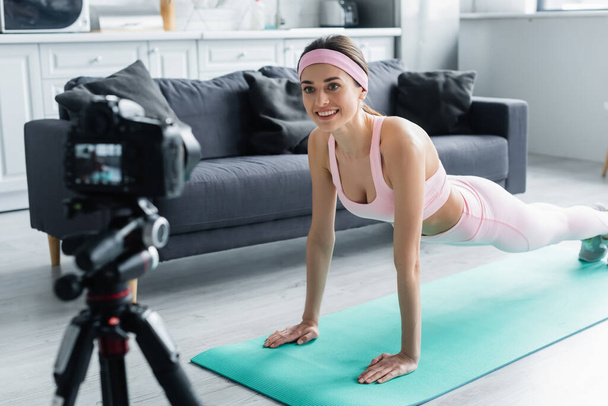 happy sports blogger training in plank pose in front of blurred digital camera - Foto, Bild