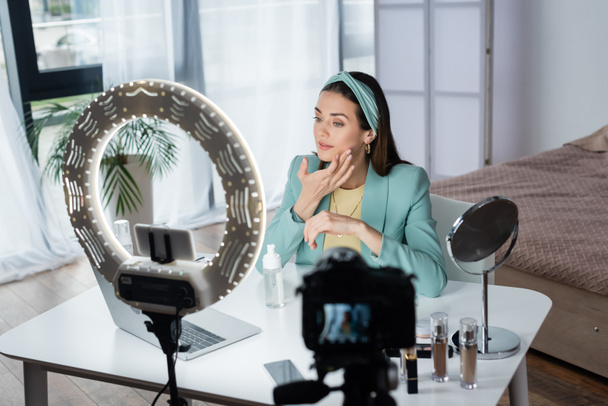 bastante belleza blogger aplicando espuma facial cerca de dispositivos y lámpara de anillo - Foto, Imagen