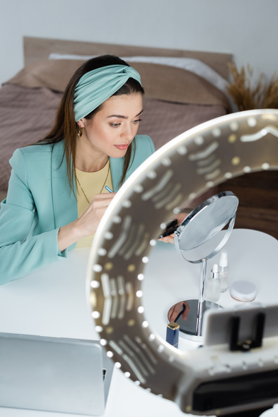 стильный блогер красоты рядом зеркало, ноутбук и телефон держатель с кругом света - Фото, изображение
