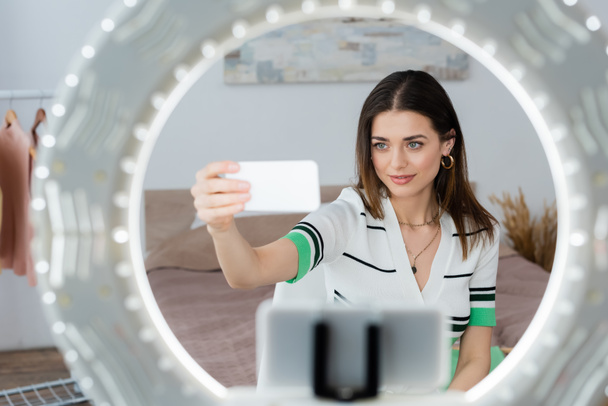 niewyraźne uchwyt telefonu z lampą pierścień w pobliżu blogger mody robi selfie na smartfonie - Zdjęcie, obraz