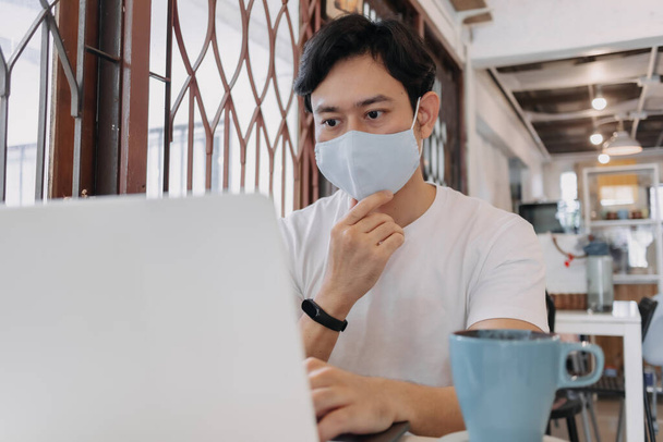Man work in cafe with mask on the face. Concept of freelance with Covid. - Фото, изображение