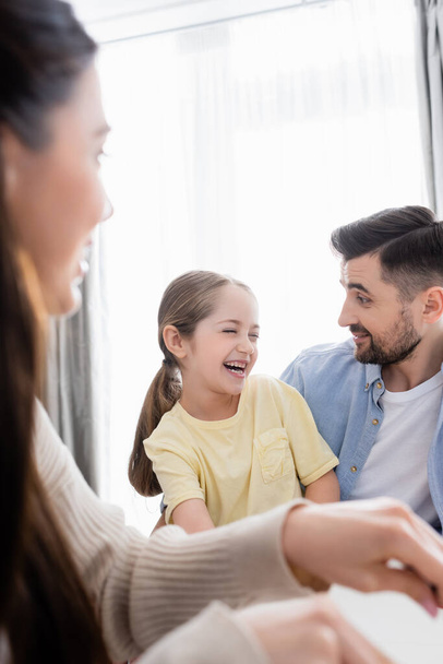 cheerful girl laughing near happy dad and blurred mother - Photo, Image