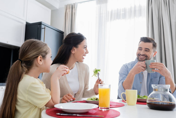 cheerful couple smiling during breakfast with daughter in kitchen - Fotoğraf, Görsel