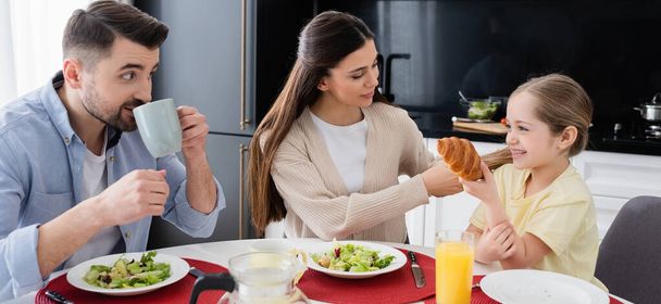 woman braiding hair of daughter near husband drinking coffee during breakfast, banner - Photo, Image