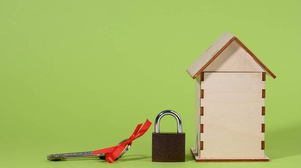 casa de madera en miniatura y cerradura de metal sobre un fondo verde, concepto de seguridad. Propiedad privada - Foto, Imagen