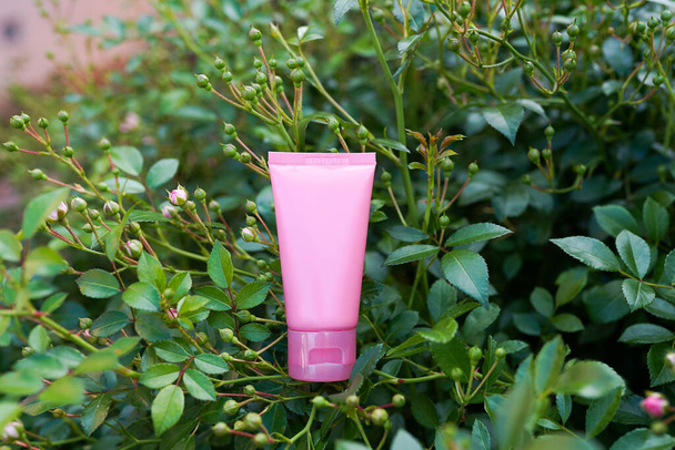 La crema cosmética natural para el cuidado del cuerpo sobre las hojas verdes. tubo rosa con cosméticos orgánicos de plantas para el cuidado de la piel - Foto, Imagen
