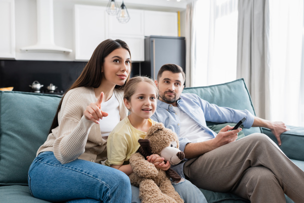 woman pointing with finger while watching tv with husband and daughter - Φωτογραφία, εικόνα