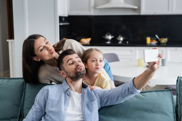 genitori con figlia che fa il broncio alle labbra mentre scattano selfie sul cellulare a casa - Foto, immagini