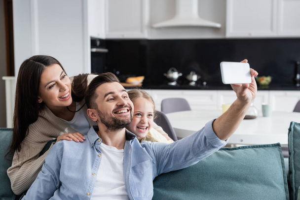 cheerful man taking selfie on cellphone with happy wife and daughter - Photo, image