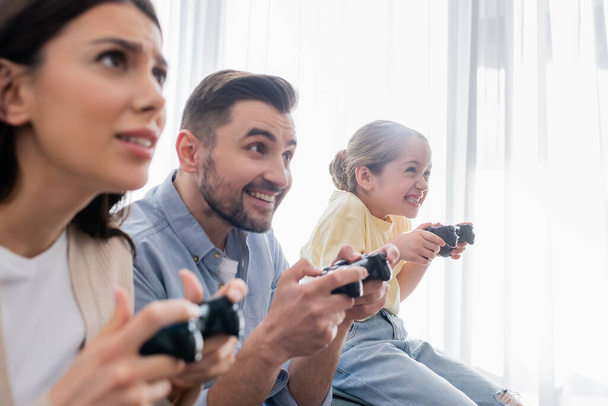 KYIV, UKRAINE - APRIL 8, 2021: excited family gaming with joysticks together on blurred foreground - Photo, image
