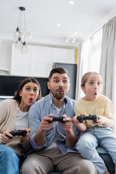 KYIV, UKRAINE - APRIL 8, 2021: astonished family playing video game together at home - Foto, afbeelding